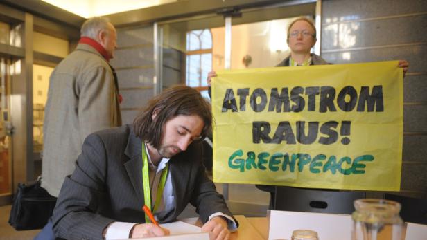 Ein Mann unterschreibt eine Petition vor einem „Atomstrom Raus!“-Banner von Greenpeace.