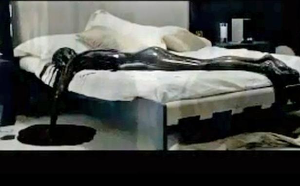 Eine mit dunkler Flüssigkeit bedeckte Person liegt auf einem Bett.