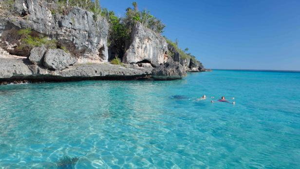Zwei Personen schwimmen im türkisfarbenen Wasser vor einer felsigen Küste.
