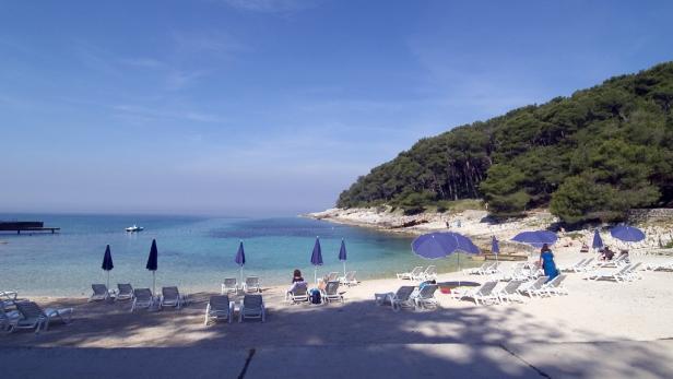 Ein Strand mit Liegestühlen und Sonnenschirmen an einem sonnigen Tag.