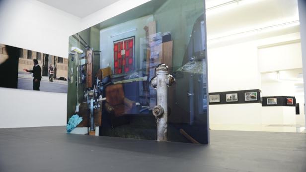 In einer Galerie steht eine große Fotografie mit einer Innenraumszene und einem Hydranten.
