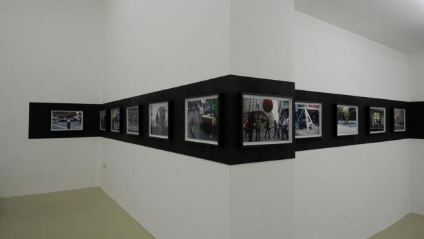 Eine Reihe gerahmter Fotografien hängt an einer schwarzen Leiste in einem Ausstellungsraum.