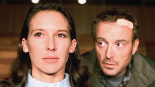 Eine Frau mit langen braunen Haaren und ein Mann mit einem Pflaster auf der Stirn schauen aufmerksam.