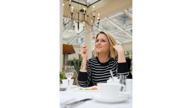 Eine Frau sitzt an einem Tisch in einem Wintergarten und isst eine Karotte.