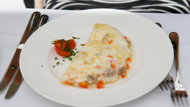 Ein Omelett mit Gemüse auf einem weißen Teller, garniert mit Tomaten und Petersilie.