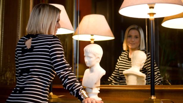 Eine Frau betrachtet eine Büste vor einem Spiegel.