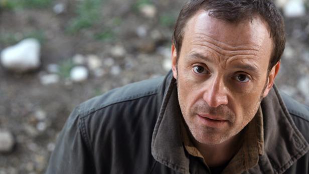 Ein Mann mit braunen Haaren und einer grünen Jacke blickt nach oben.