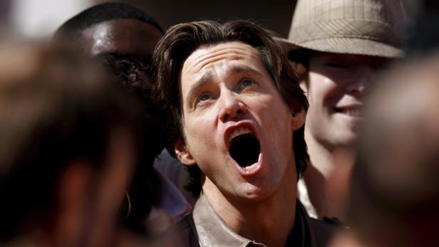 Jim Carrey schreit mit offenem Mund, umgeben von anderen Menschen.