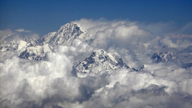 Schneebedeckte Berggipfel ragen aus einer Wolkendecke in den blauen Himmel.