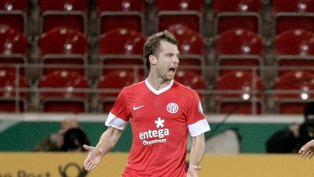 Ein Fußballspieler in rotem Trikot gestikuliert auf dem Spielfeld.