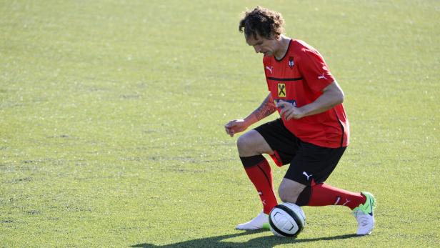 Ein Fußballspieler mit Tätowierung kniet auf dem Rasen neben einem Fußball.