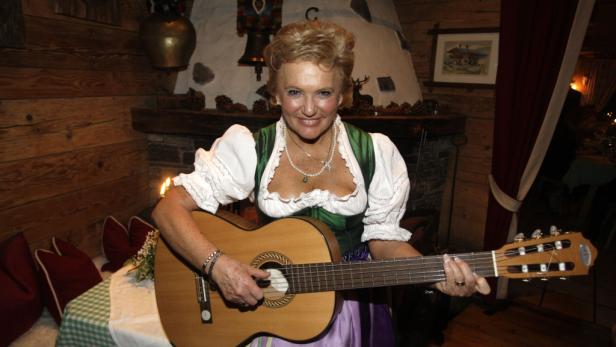 Eine Frau im Dirndl spielt Gitarre in einer rustikalen Hütte.