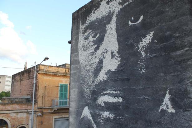 Ein großes Graffito-Porträt an einer Hauswand in einer Stadt.