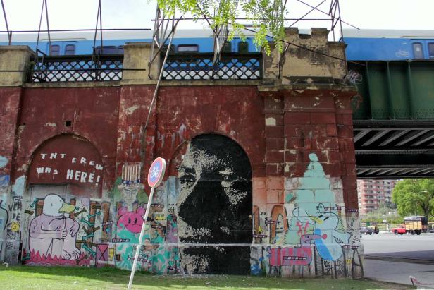 Eine mit Graffiti bemalte Brücke mit einem Porträt und einem Zug im Hintergrund.