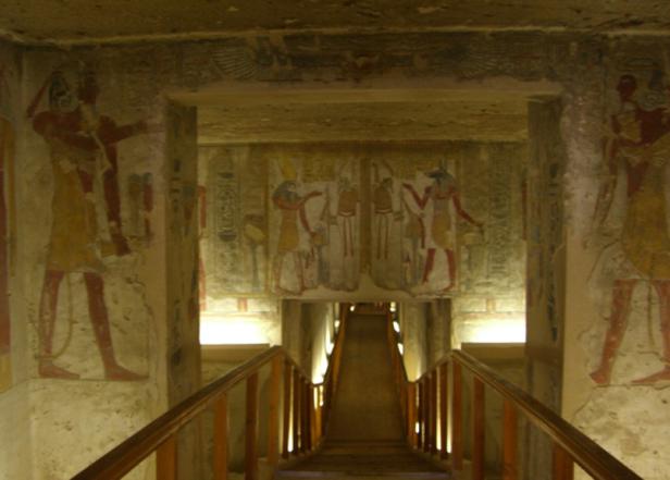 Blick in das Innere eines ägyptischen Grabes mit bemalten Wänden und einer Treppe.
