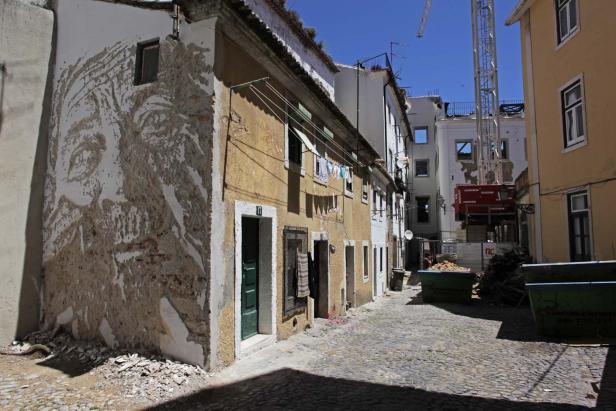 In einer Gasse steht ein Haus mit einem großen Gesicht an der Fassade.