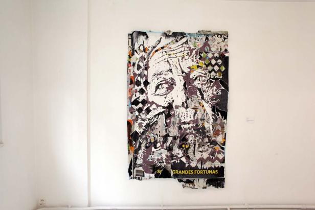 Ein zerfetztes Poster an einer Wand zeigt das Gesicht eines alten Mannes.