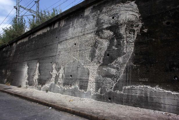 Ein Betonwandgemälde zeigt ein Gesicht und mehrere Figuren.
