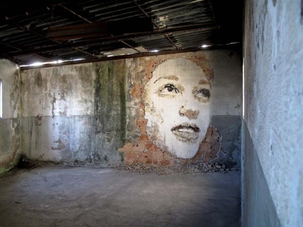 Ein Porträt einer Frau ist auf eine verfallene Ziegelwand gemalt.