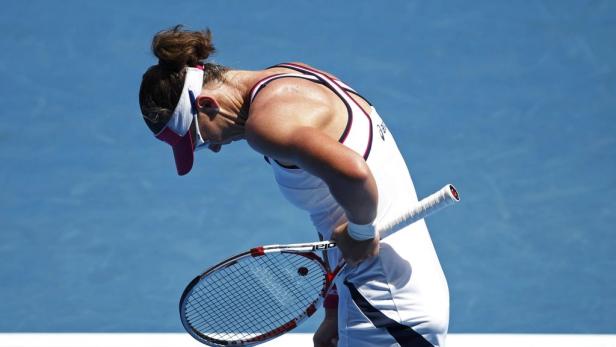 Eine Tennisspielerin mit gesenktem Kopf hält ihren Schläger.