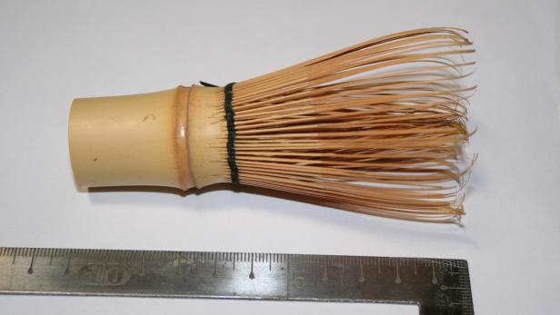 Ein Matcha-Besen aus Bambus liegt neben einem Lineal.