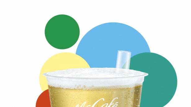 Ein McCafé-Getränk mit Schaum und einem kleinen Glas auf dem Deckel vor bunten Kreisen.