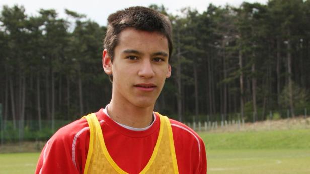 Ein junger Mann mit rotem T-Shirt und gelber Trainingsweste steht im Freien.