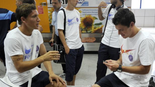 Zwei junge Männer mit T-Shirts einer Fußballmannschaft sitzen in einem Wartebereich.