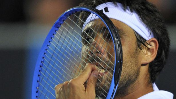 Ein Tennisspieler mit Stirnband kaut auf seinem Tennisschläger.