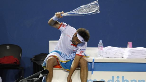 Ein Tennisspieler sitzt erschöpft auf einer Bank und hält einen Schläger in der Hand.