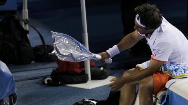 Ein Tennisspieler sitzt und hält einen neuen, verpackten Tennisschläger.