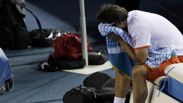 Ein Tennisspieler sitzt erschöpft mit einem Handtuch im Gesicht auf der Bank.