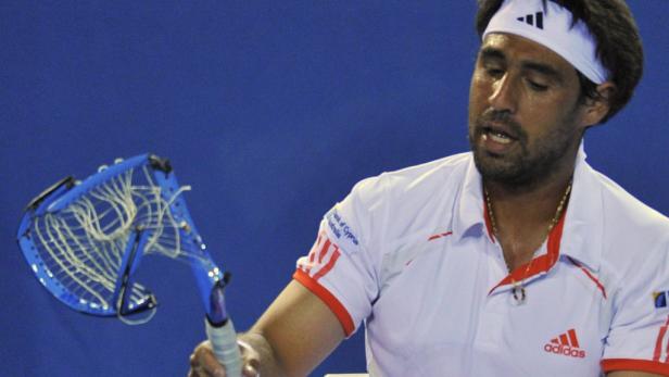 Ein Tennisspieler mit Stirnband hält einen beschädigten Tennisschläger in der Hand.