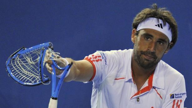 Ein Tennisspieler mit Stirnband hält einen beschädigten Tennisschläger in der Hand.