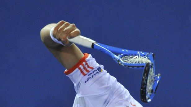 Ein Tennisspieler schlägt einen Ball mit einem blauen Tennisschläger.