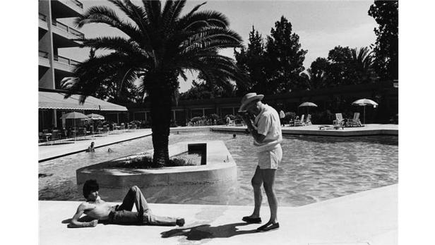 Ein Mann fotografiert eine andere Person, die am Pool liegt.