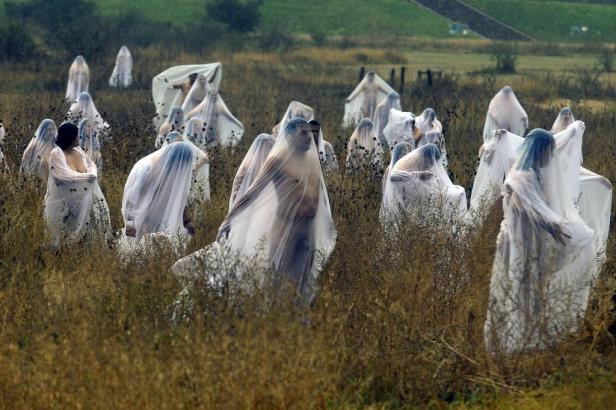 Eine Gruppe von Menschen, gehüllt in weiße Stoffe, steht auf einem Feld.