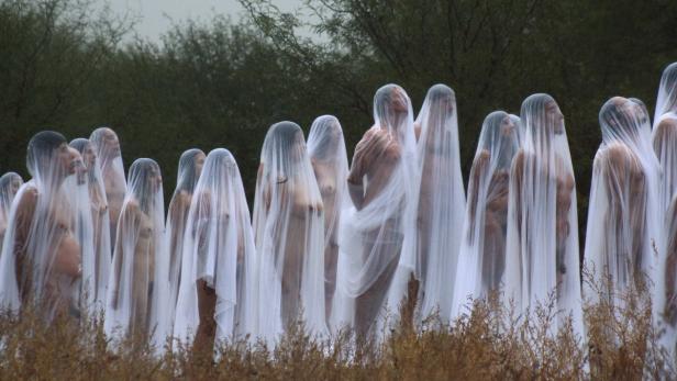 Eine Gruppe von Menschen steht mit weißen Tüchern bedeckt in einer Landschaft.