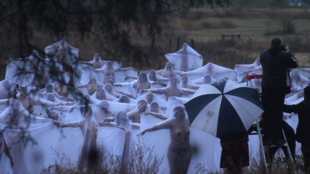 Eine Gruppe von Menschen, mit Tüchern bedeckt, steht auf einem Feld, während sie fotografiert werden.