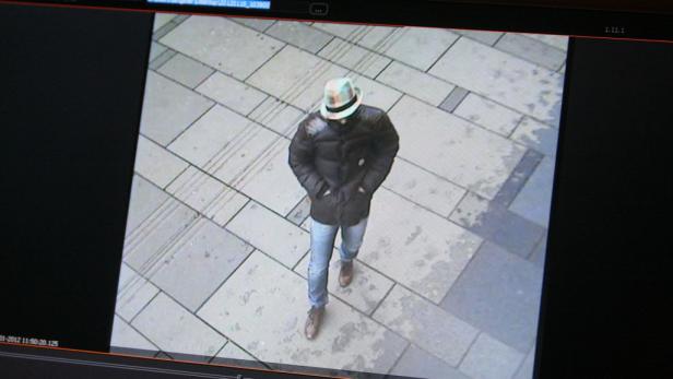 Eine Person mit Hut, dunkler Jacke und Jeans geht auf einem gepflasterten Weg.