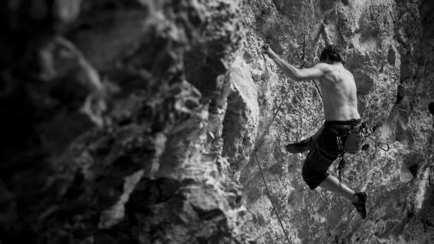 Ein Mann klettert in Schwarzweiß an einer steilen Felswand.