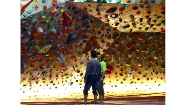 Zwei Männer stehen vor einer Kletterwand mit bunten Griffen.