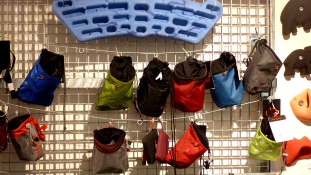 Verschiedene Chalkbags hängen an einer Gitterwand, darunter ein blaues Trainingsboard.