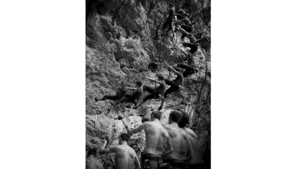 Ein Kletterer wird von mehreren Personen am Fuße einer Felswand gesichert.