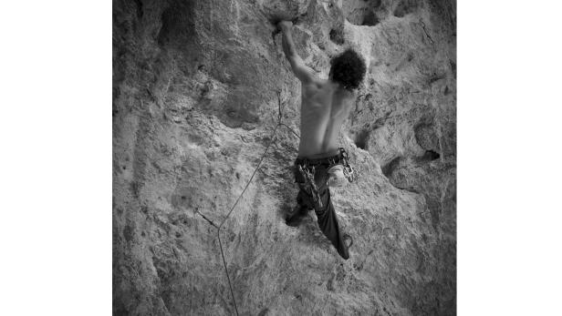 Ein Mann klettert in Schwarzweiß eine steile Felswand hoch.