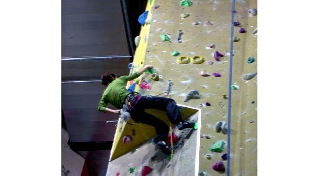 Eine Person klettert an einer Kletterwand mit farbigen Griffen.