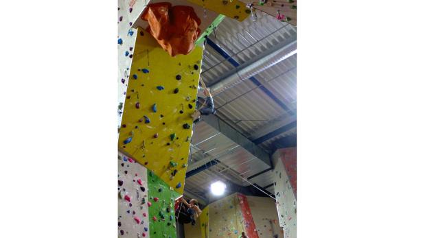 Zwei Personen klettern an einer bunten Kletterwand in einer Halle.