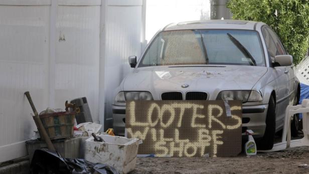 Ein silberner BMW steht vor einer Wand, davor ein Schild mit der Aufschrift „Looters will be shot!“.