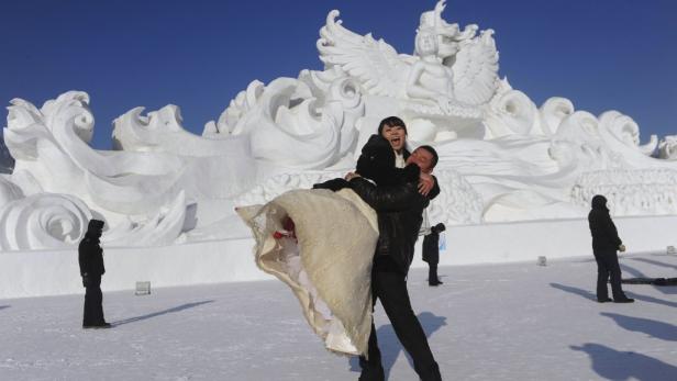 Ein Paar posiert vor einer großen Schneeskulptur für ein Hochzeitsfoto.