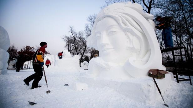 Mehrere Personen arbeiten an einer großen Schneeskulptur eines Frauengesichts.